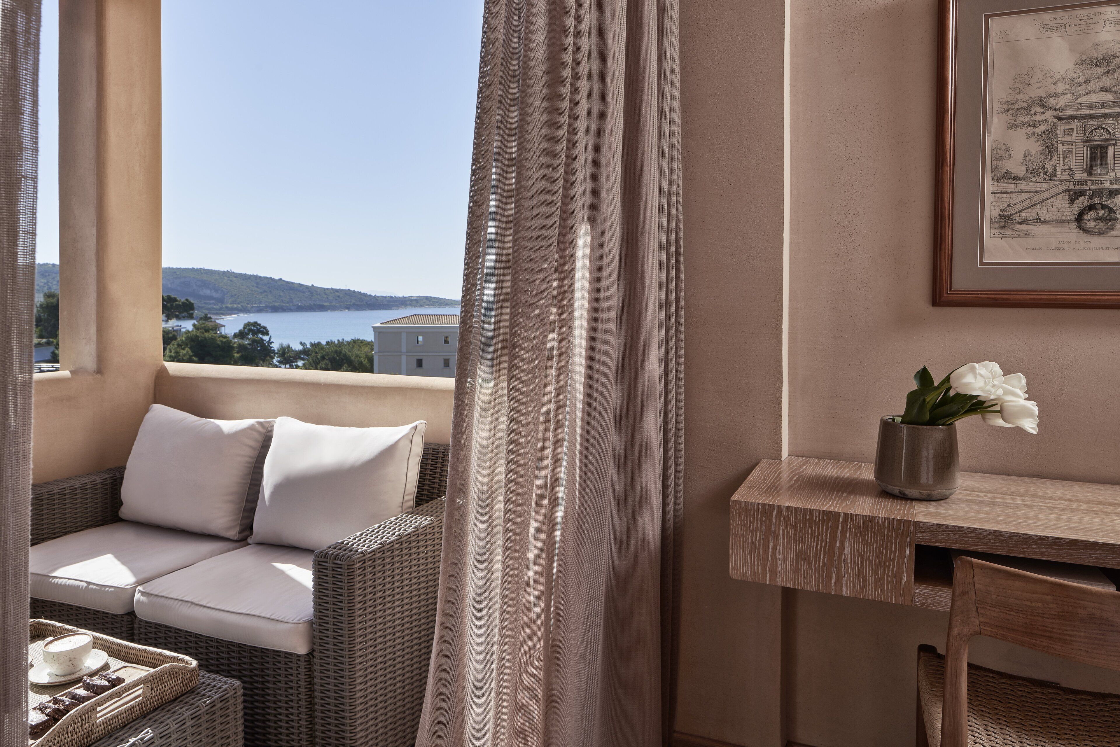 Un balcon avec un canapé en osier, une petite table et un tableau encadré accroché au mur.
