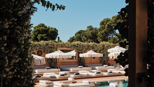 A poolside area with sun loungers and umbrellas, surrounded by greenery and trees. - The Margi (Vari-Voula-Vouliagmeni)