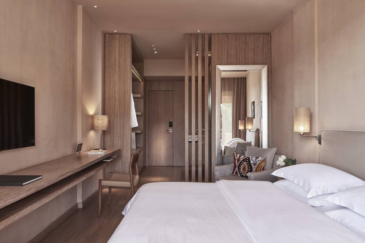 A modern hotel room with a large bed, a desk, a chair, and a TV.