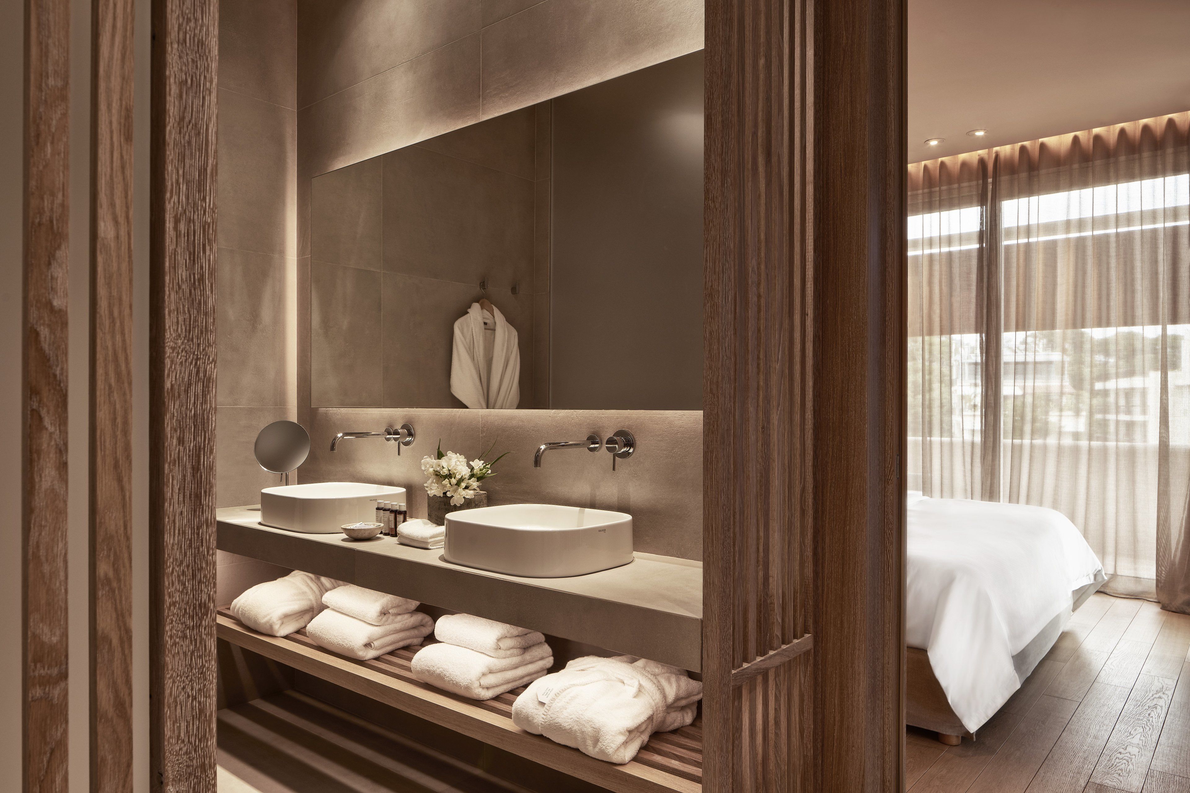 A modern bathroom with two sinks, a large mirror, and a vanity with neatly folded towels.
