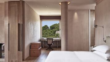 A modern bedroom with a large bed, a desk with a chair, and a view of greenery outside.