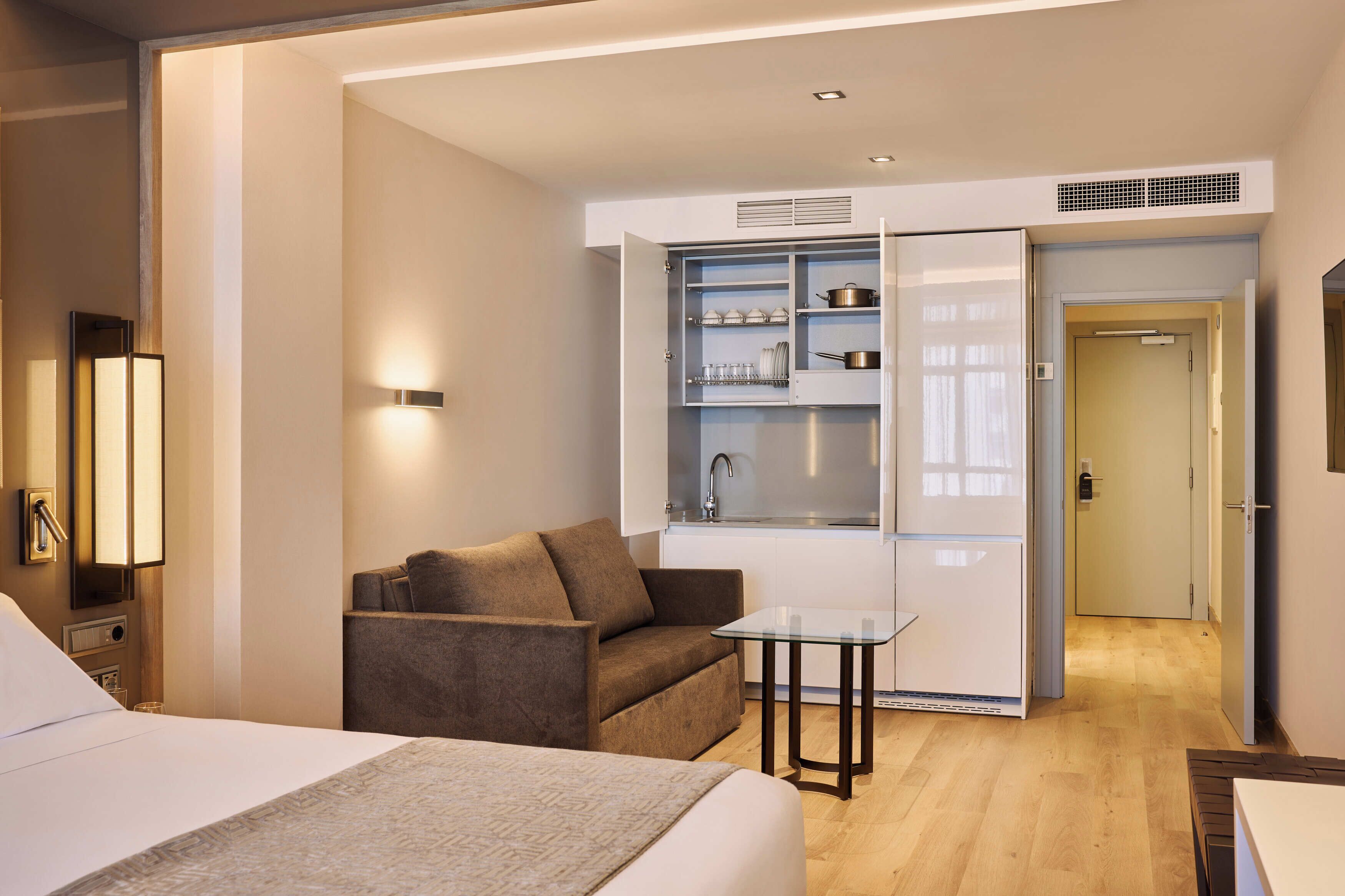Une chambre d’hôtel avec un lit, un canapé, une table en verre et une kitchenette.