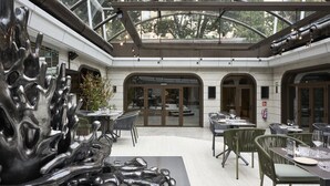 A modern indoor dining area with tables and chairs, a large abstract sculpture, and a glass ceiling. - VP SOGNIO Madroño (Madrid)