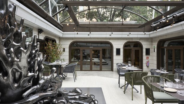 Un comedor interior moderno con mesas, sillas y una gran escultura abstracta, además de un techo de cristal.