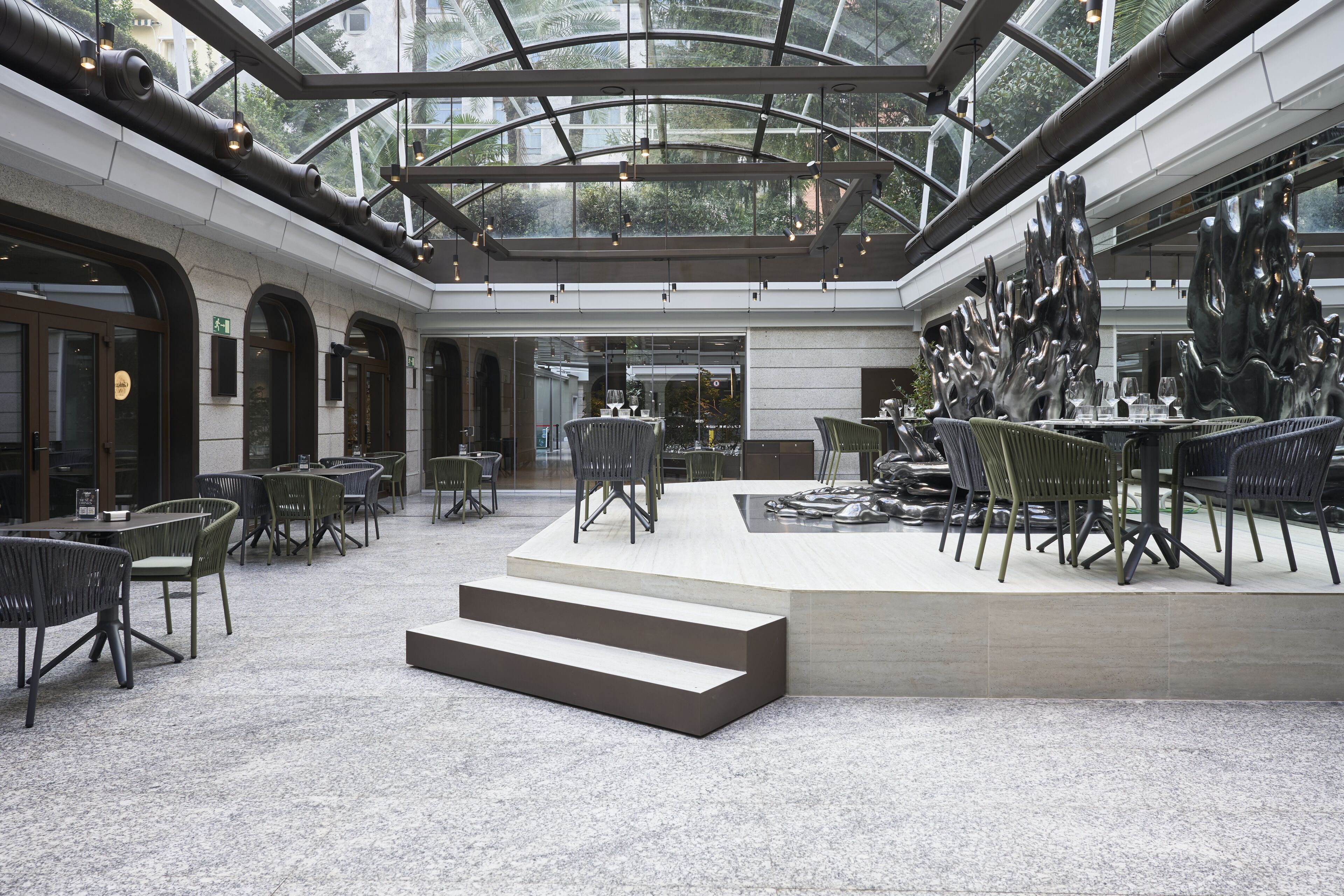 A spacious indoor area with a glass ceiling, modern furniture, and a central seating area.