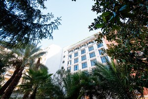 Un edificio de varios pisos con estilo arquitectónico moderno, rodeado de exuberante vegetación, incluyendo palmeras.