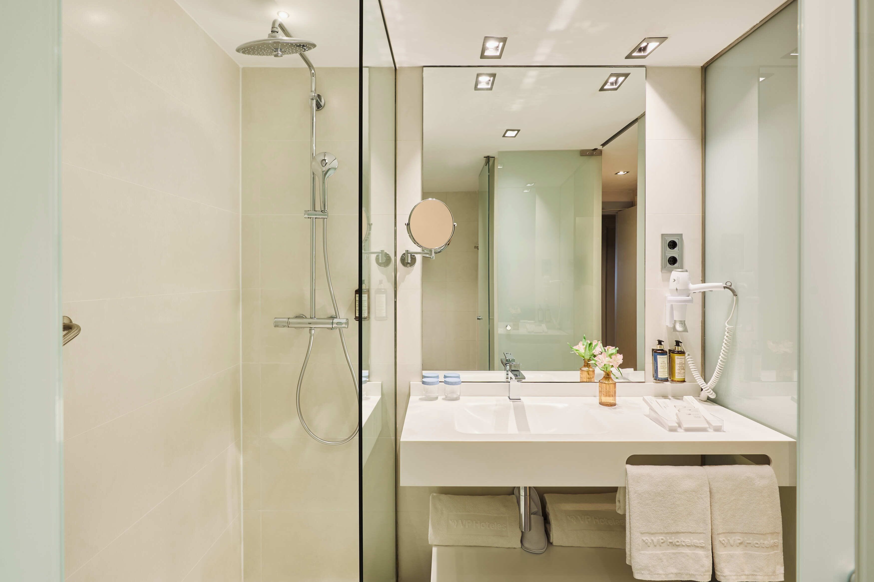 Un baño moderno con ducha envuelta en vidrio, tocador con espejo y perchero.