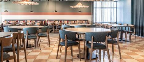 A modern dining area with round tables, blue upholstered chairs, and unique pendant lighting.