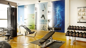 A gym with exercise equipment, a bench, a wall with fitness posters, and a rack of dumbbells. - Scandic Espoo (Espoo)