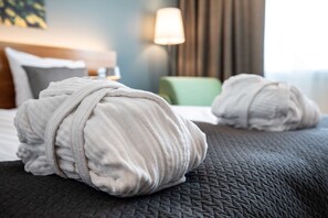 A neatly made bed with a dark gray quilt and two rolled white towels placed on it. - Scandic Espoo (Espoo)