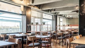 A spacious restaurant with wooden tables and chairs, large windows, and potted plants. - Scandic Espoo (Espoo)