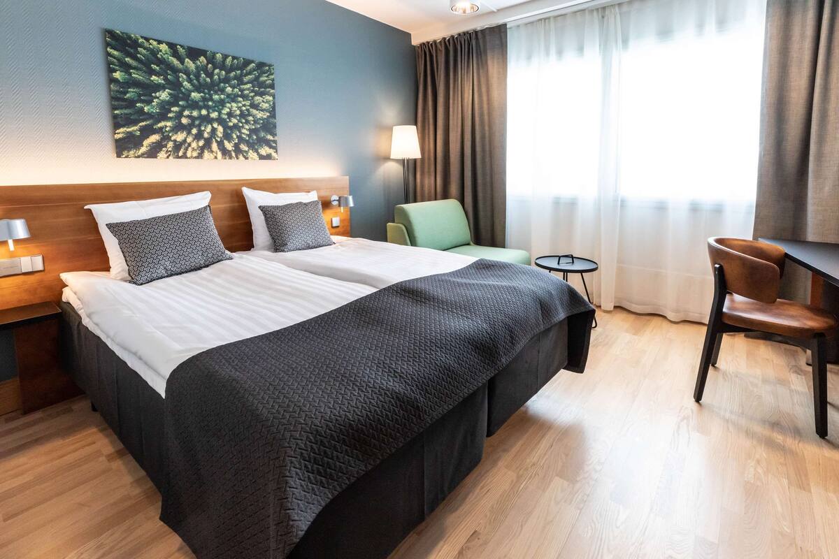 Hotellihuone, jossa on suuri sänky, työpöytä, tuoli ja lamppu.