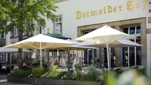 Terrasse extérieure avec parasols, un restaurant appelé « Detmolder Hof » et une façade en verre.