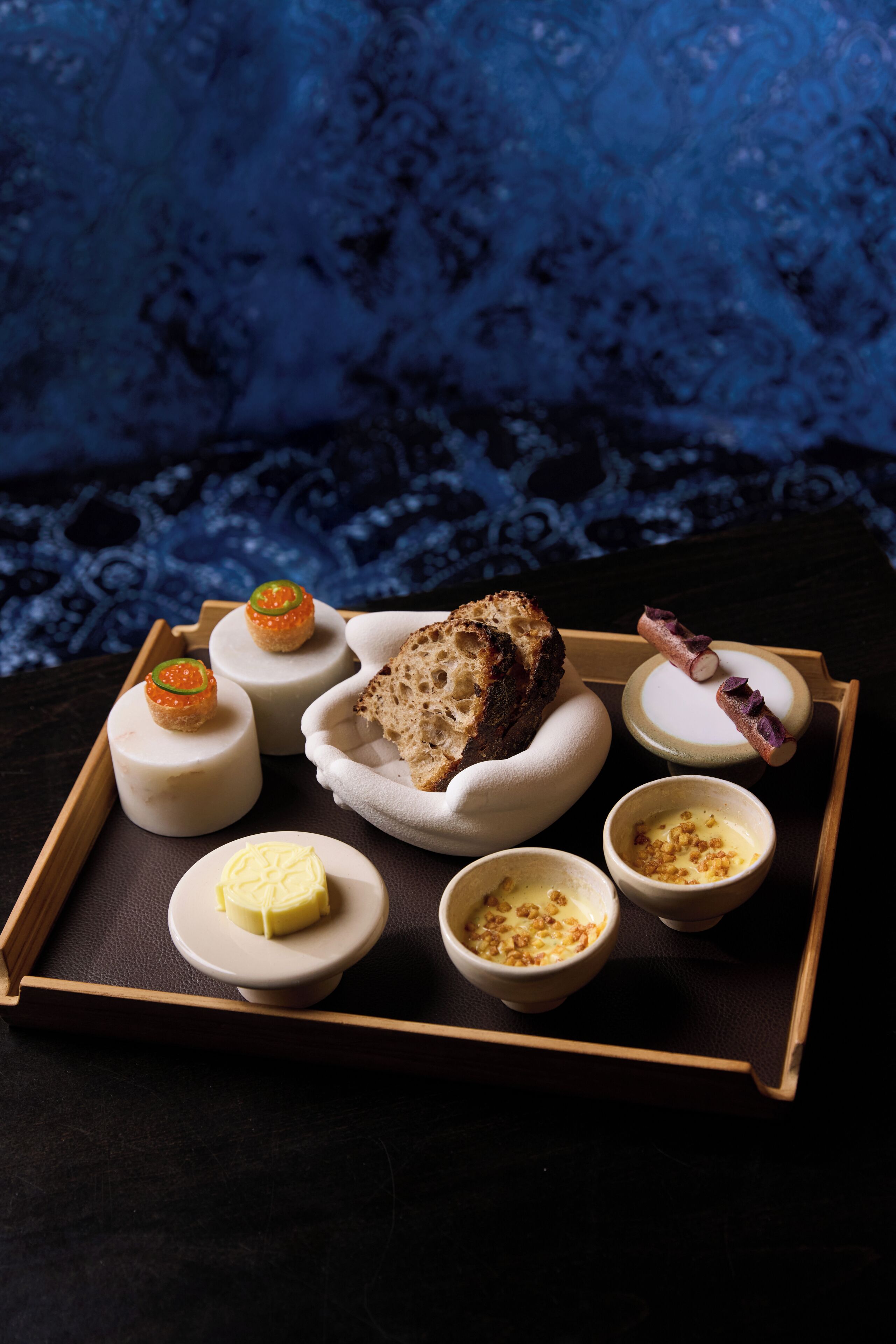 Una bandeja con distintos alimentos, incluyendo queso, pan y recipientes pequeños con salsas.