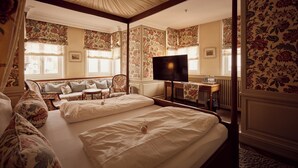 Une chambre d’hôtel avec deux lits, une télévision, une petite table et une fenêtre dont le mur est recouvert d’un papier peint à motifs floraux.