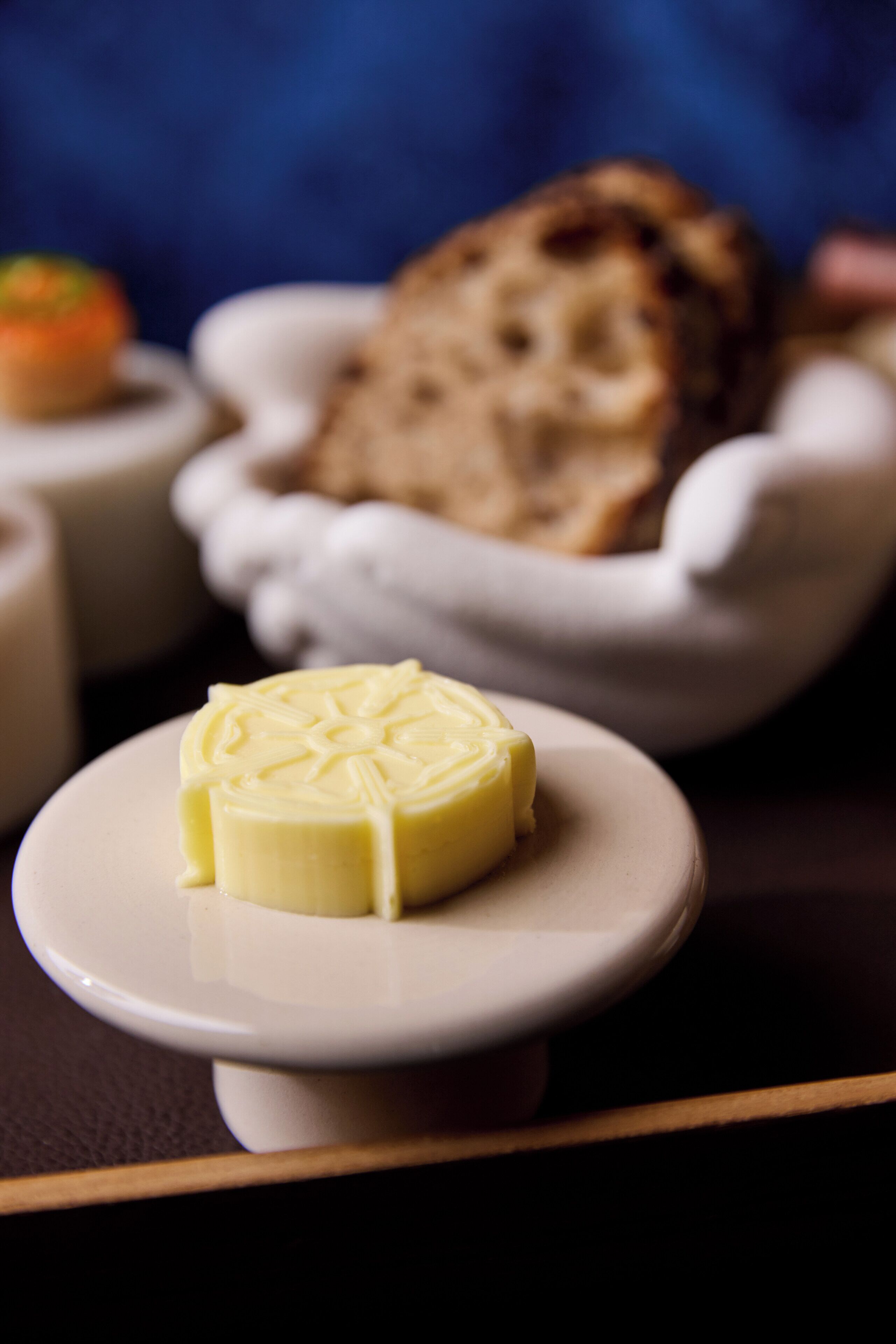 Eine Nahaufnahme einer Butterplatte mit einem Butterklotz auf einem weißen Teller, einer Brotschale und einer kleinen Schale mit einer Soße.