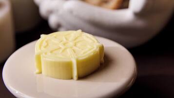 Eine Nahaufnahme einer Butterplatte mit einem Butterklotz auf einem weißen Teller, einer Brotschale und einer kleinen Schale mit einer Soße.