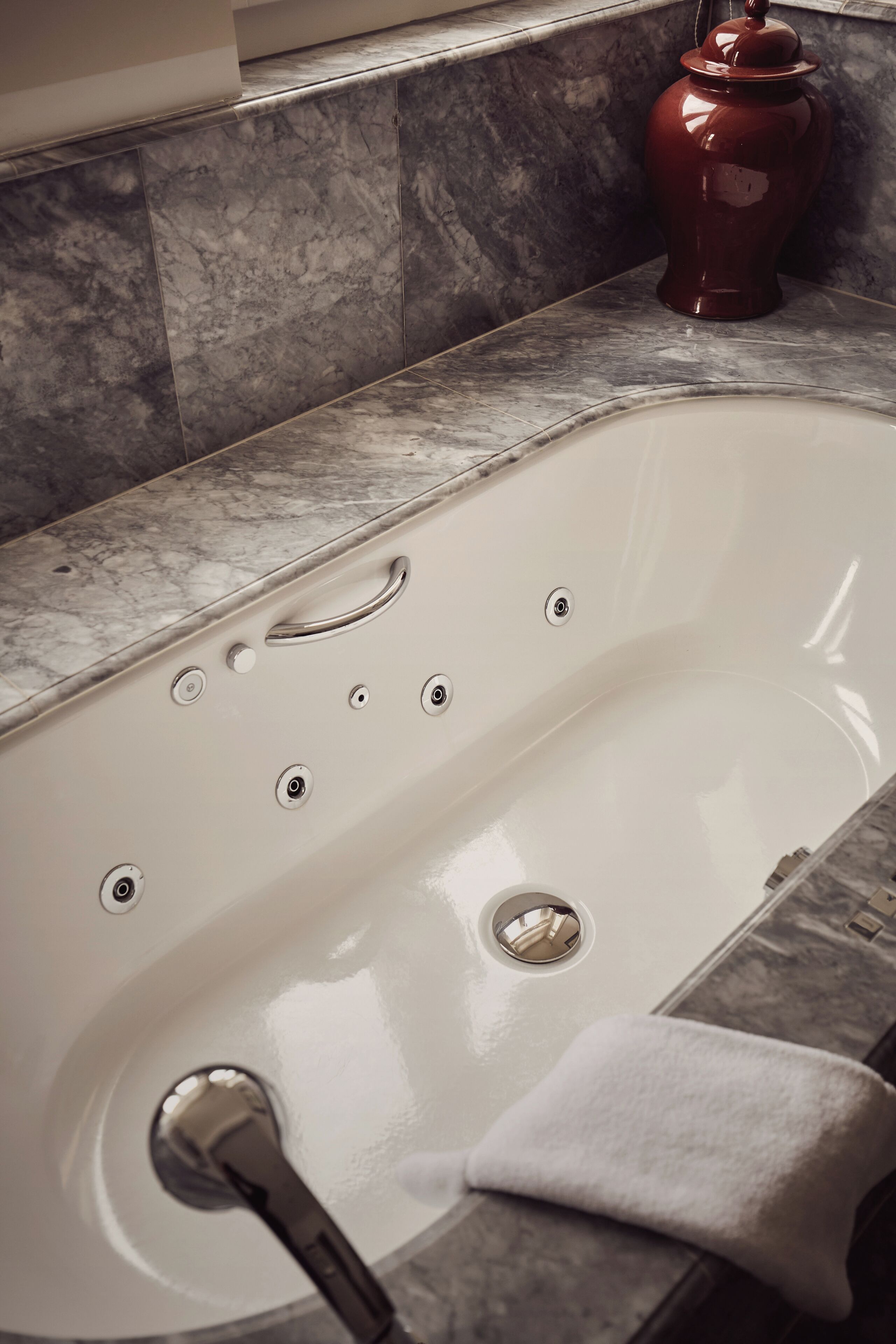 A white bathtub with multiple faucets and a drain, set against a marble countertop.