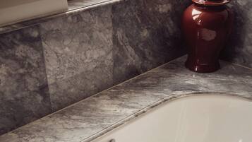 A white bathtub with multiple faucets and a drain, set against a marble countertop.