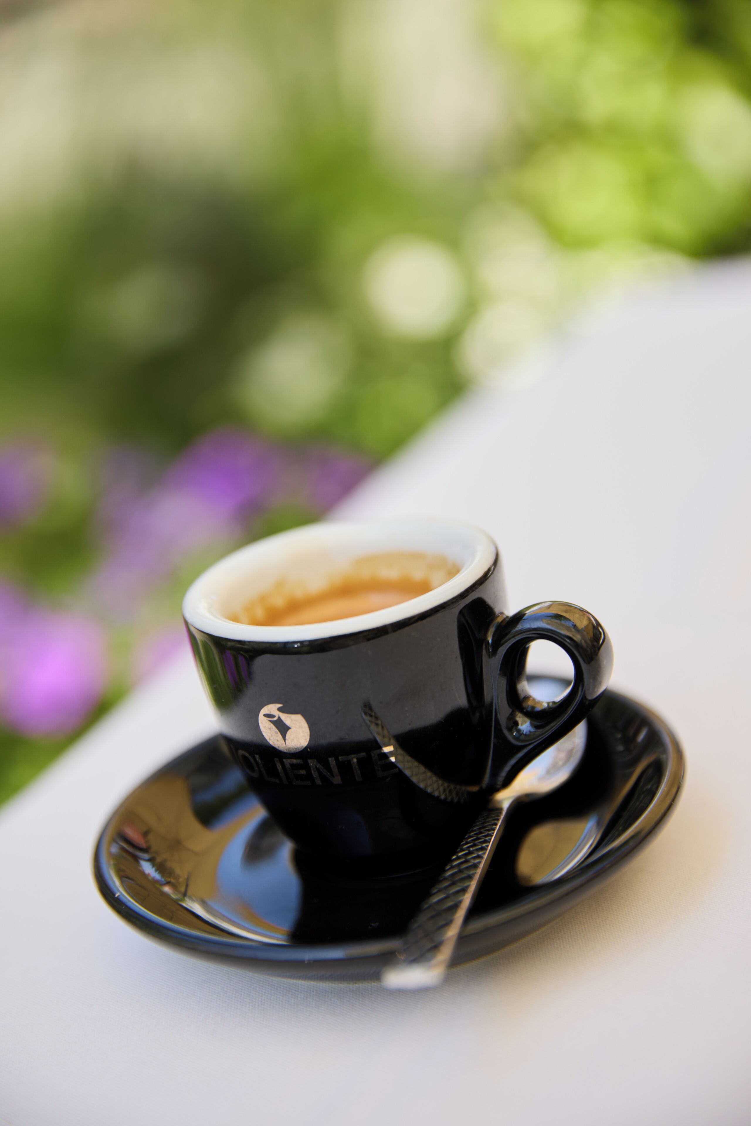A cup of coffee on a saucer with a spoon, placed on a table with a blurred green background.