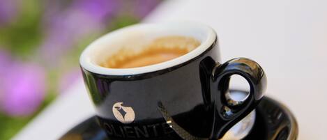 A cup of coffee on a saucer with a spoon, placed on a table with a blurred green background.