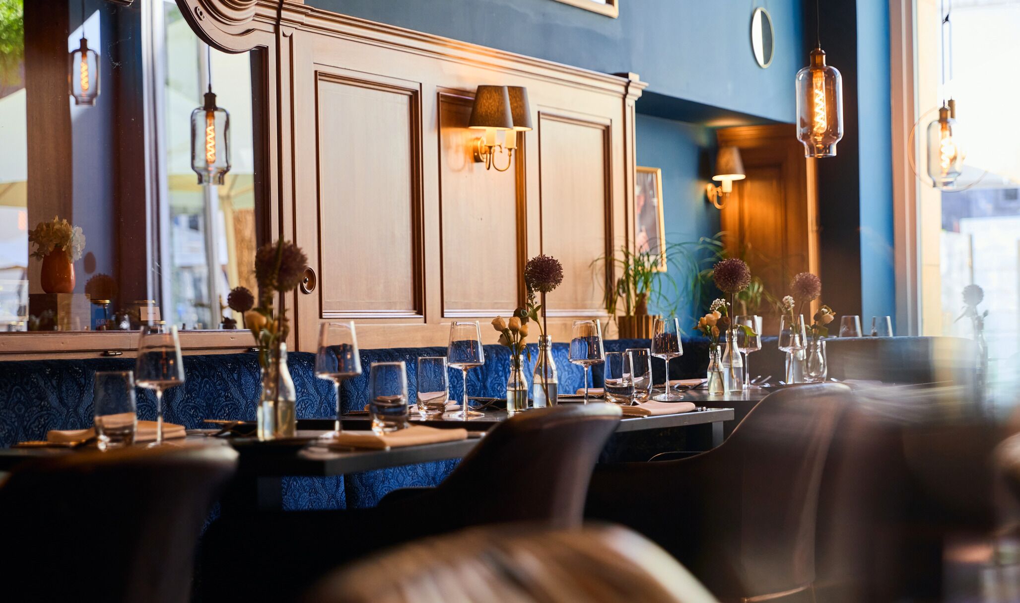 Ein Restaurantinneres mit blauer Wand mit Muster, Holzvertäfelung und einer Bar mit Gläsern und Blumen.
