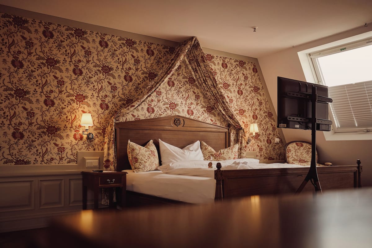A hotel room with a bed, nightstands, a TV, and a window with blinds.