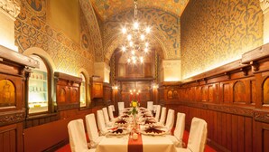 A banquet hall with a long table set for a formal event, ornate wooden paneling, and a chandelier.