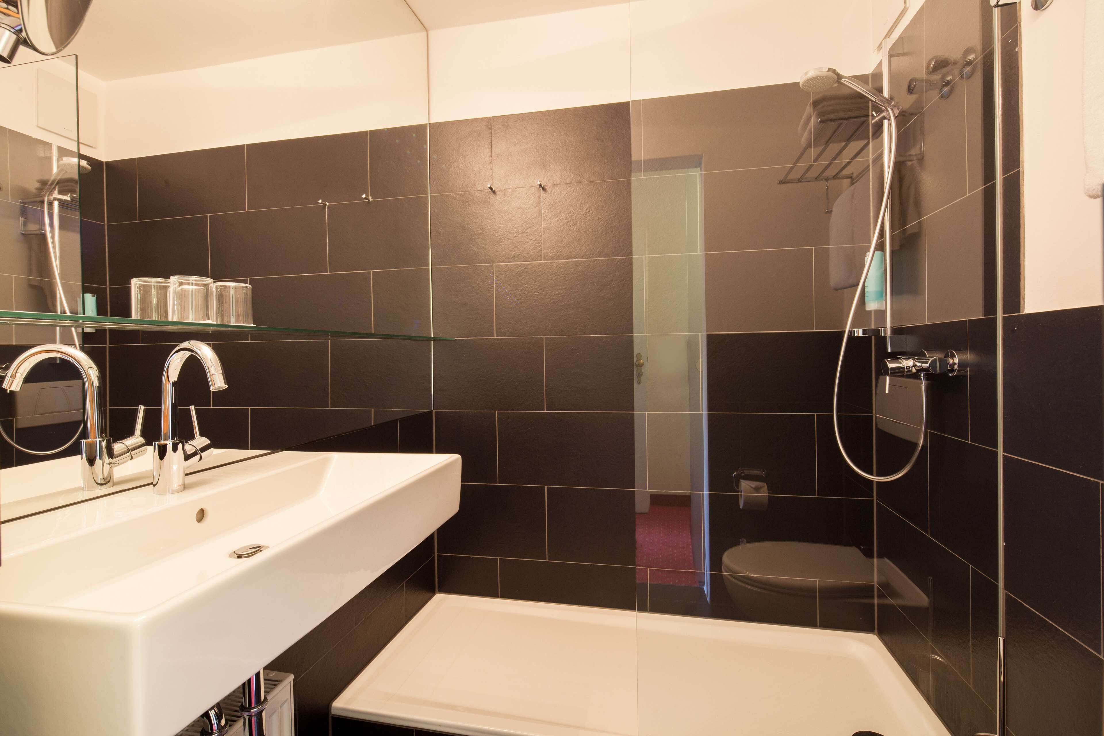 A modern bathroom with a white sink, a glass shelf, a shower, and a toilet.