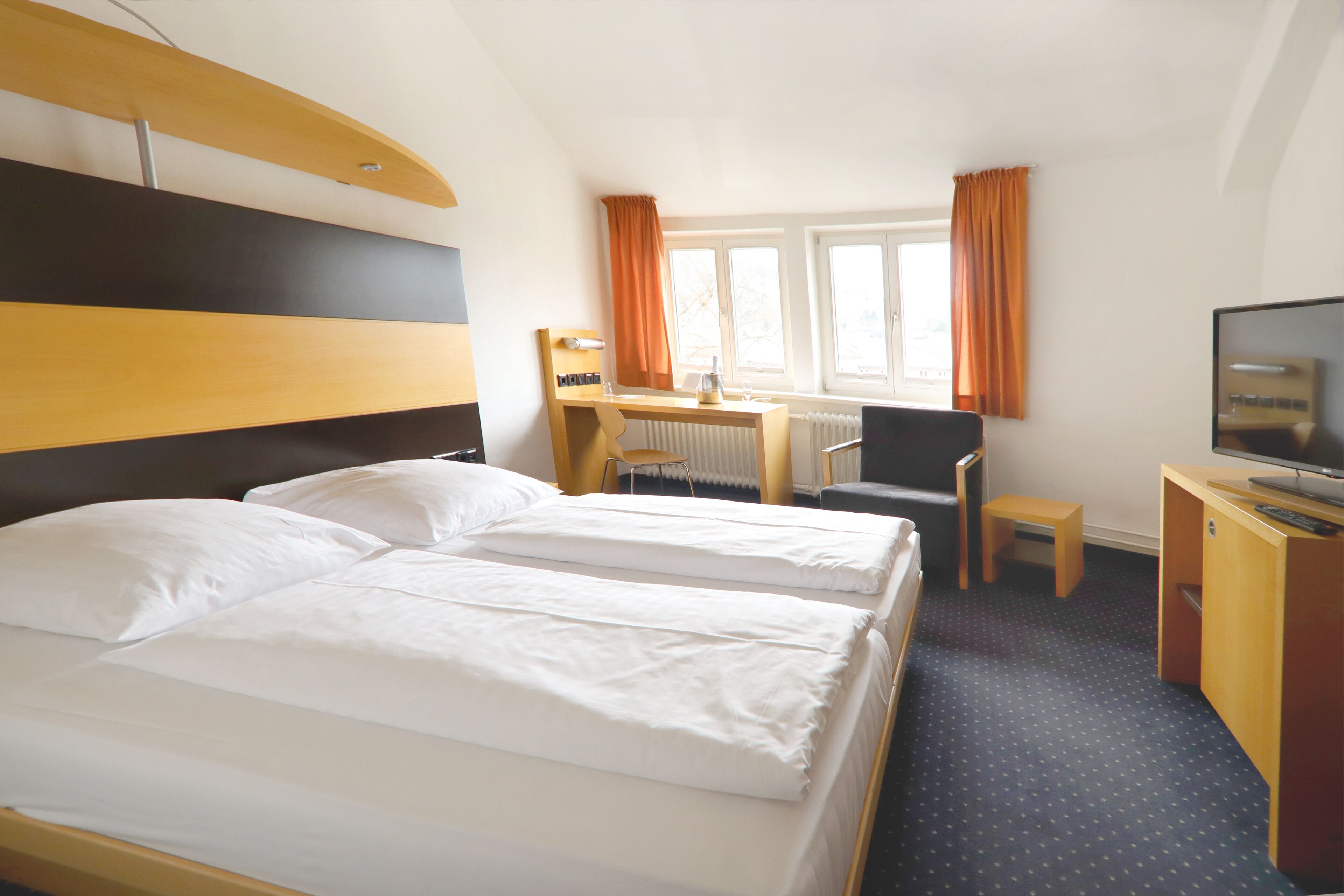 Une chambre d’hôtel avec deux lits, un bureau, une chaise, une télévision et une fenêtre avec des rideaux.