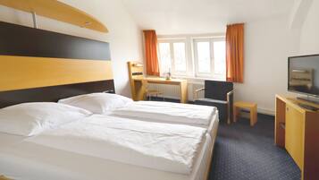 Une chambre d’hôtel avec deux lits, un bureau, une chaise, une télévision et une fenêtre avec des rideaux.