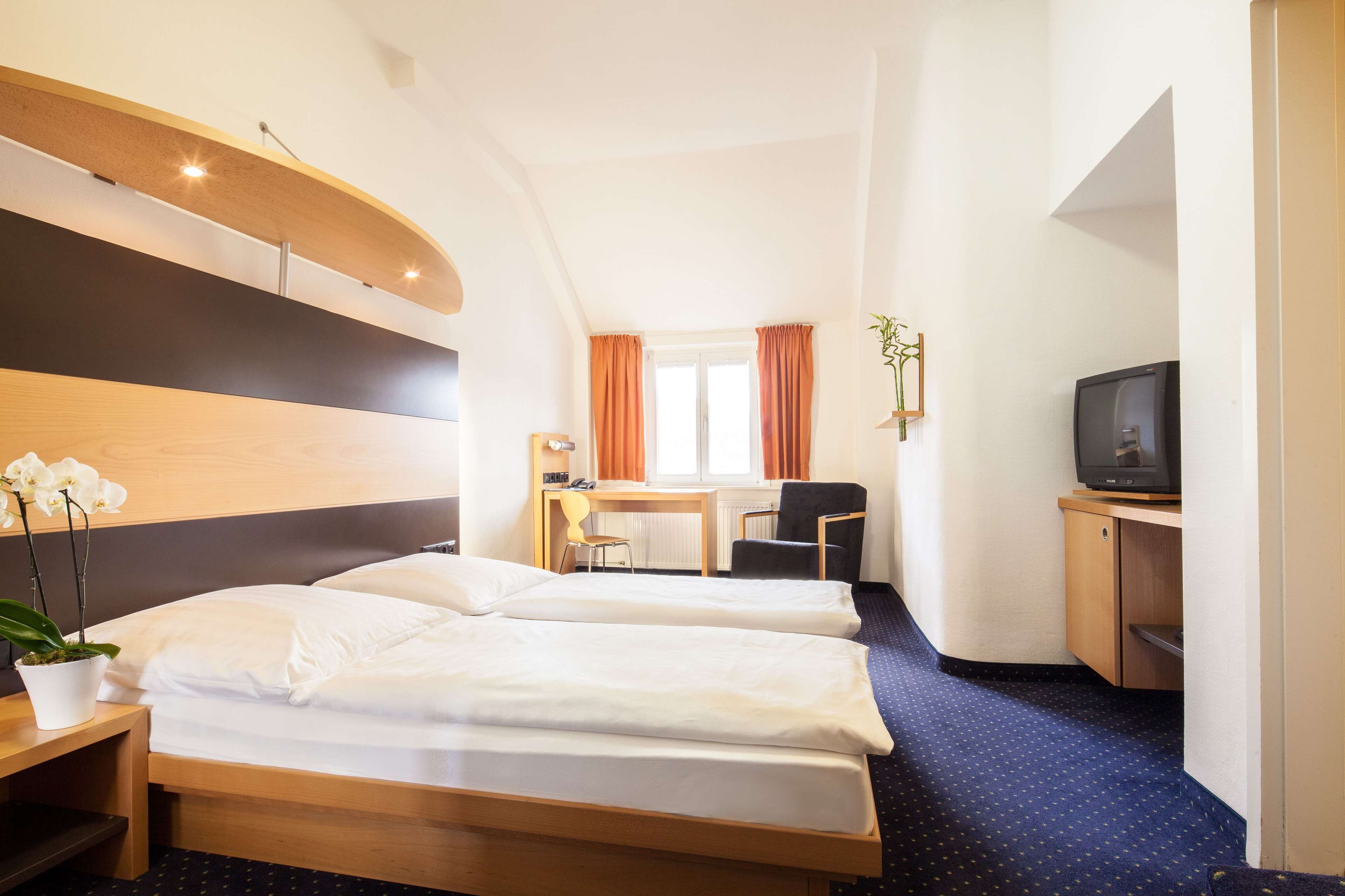 A hotel room with two beds, a desk with a chair, a television, and a potted plant.