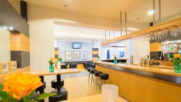 A modern bar area with wooden counters, bar stools, and a television mounted on the wall.