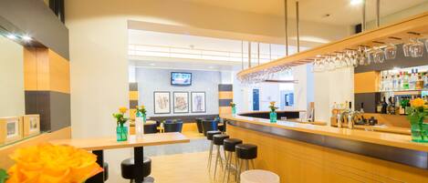 A modern bar area with wooden counters, bar stools, and a television mounted on the wall.