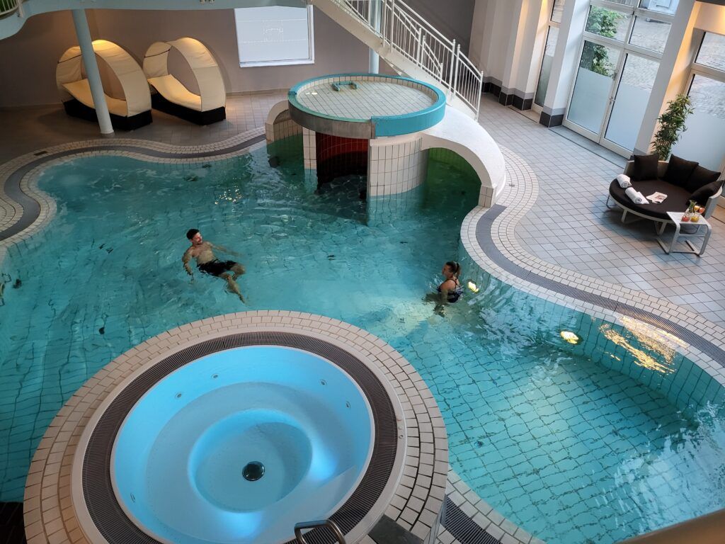 Una piscina interior con un jacuzzi central, una escalera y asientos tipo lounge.