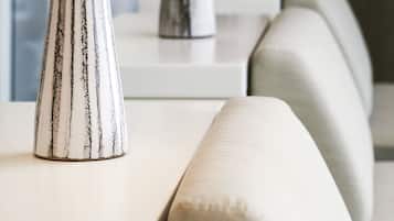 A modern hotel room with a clean, minimalist design. It features a sofa with a light fabric, a white console table, and a decorative vase.