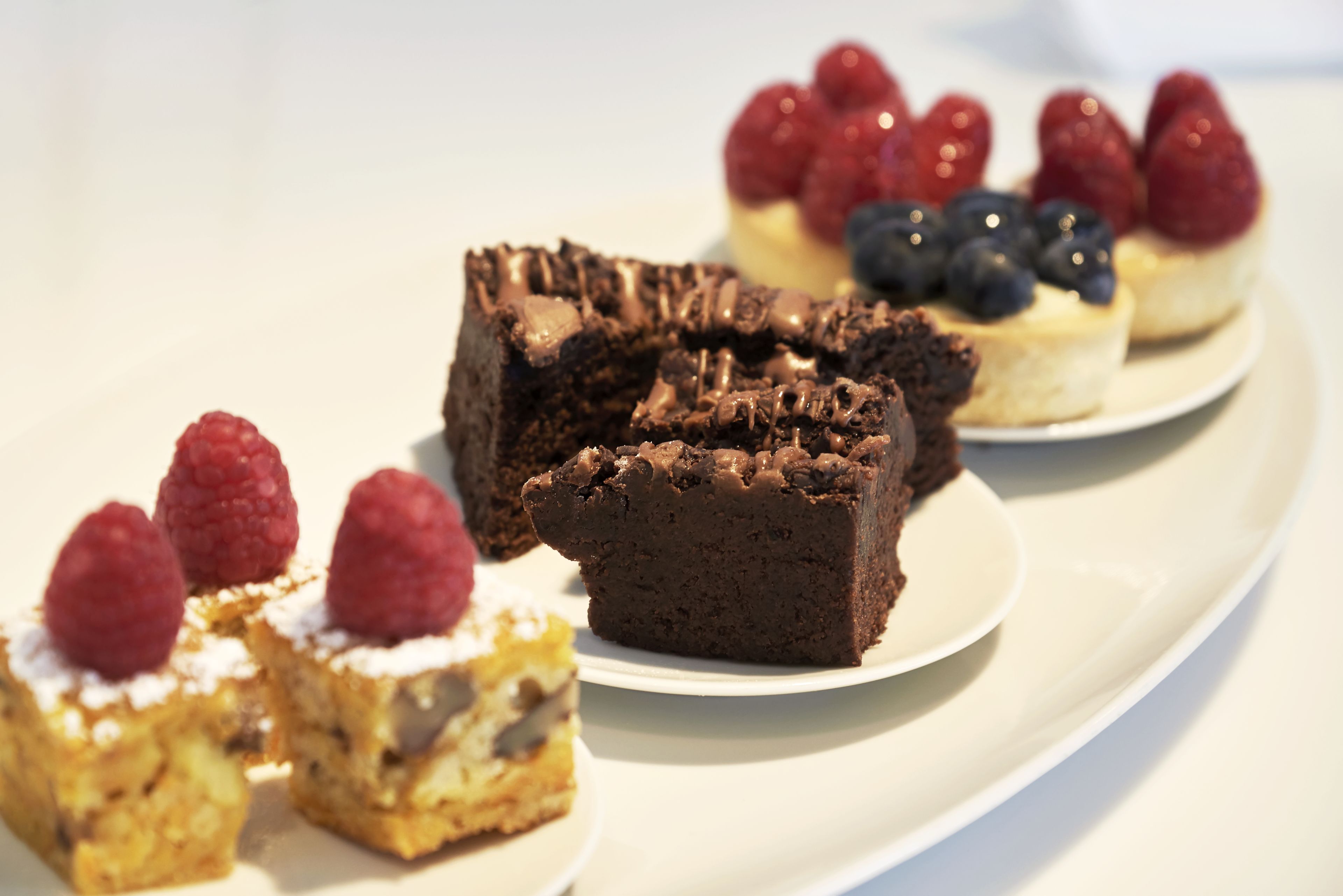 A variety of desserts on a white plate, including chocolate brownies and fruit-topped pastries.