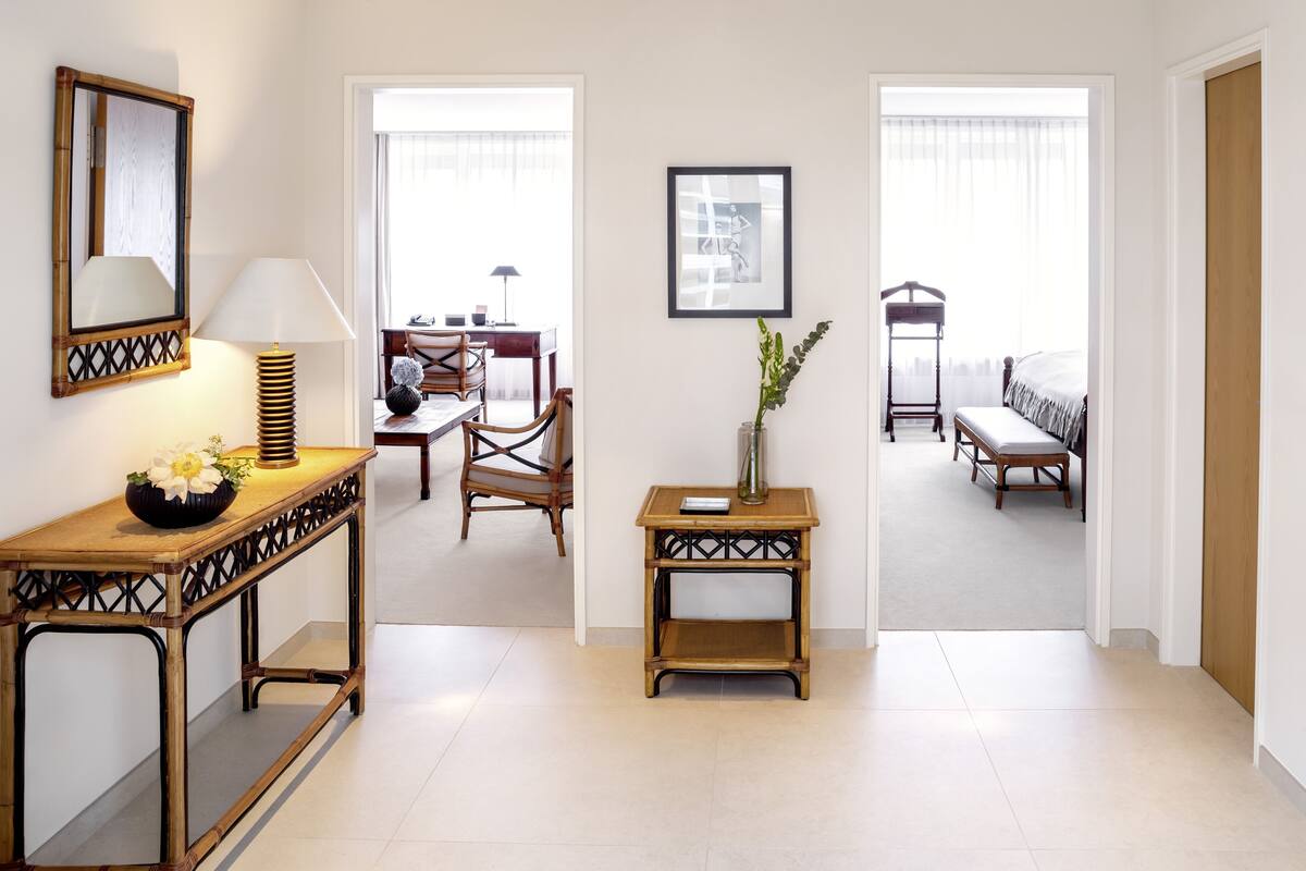 Quarto de hotel com uma mesa consola de madeira, um candeeiro, um quadro emoldurado e uma mesa de cabeceira com um vaso.