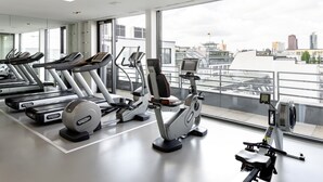 Un gimnasio con cintas de correr, elípticas y una máquina de remo, con amplias ventanas que ofrecen vistas a la ciudad.