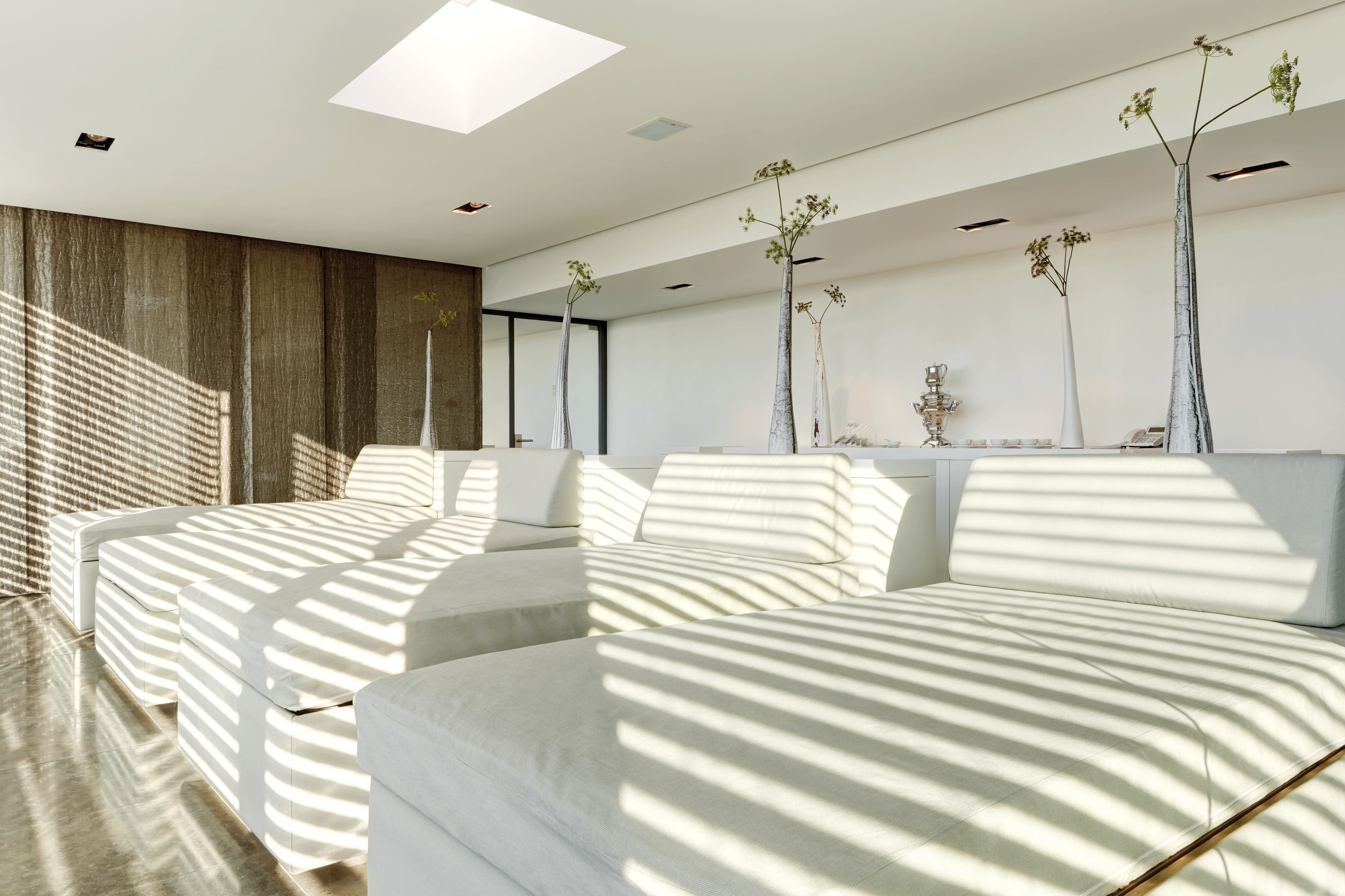 A modern bedroom with a large bed, a sofa, and a desk. There are three tall, slender vases with plants on the wall.