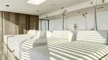 A modern bedroom with a large bed, a sofa, and a desk. There are three tall, slender vases with plants on the wall.