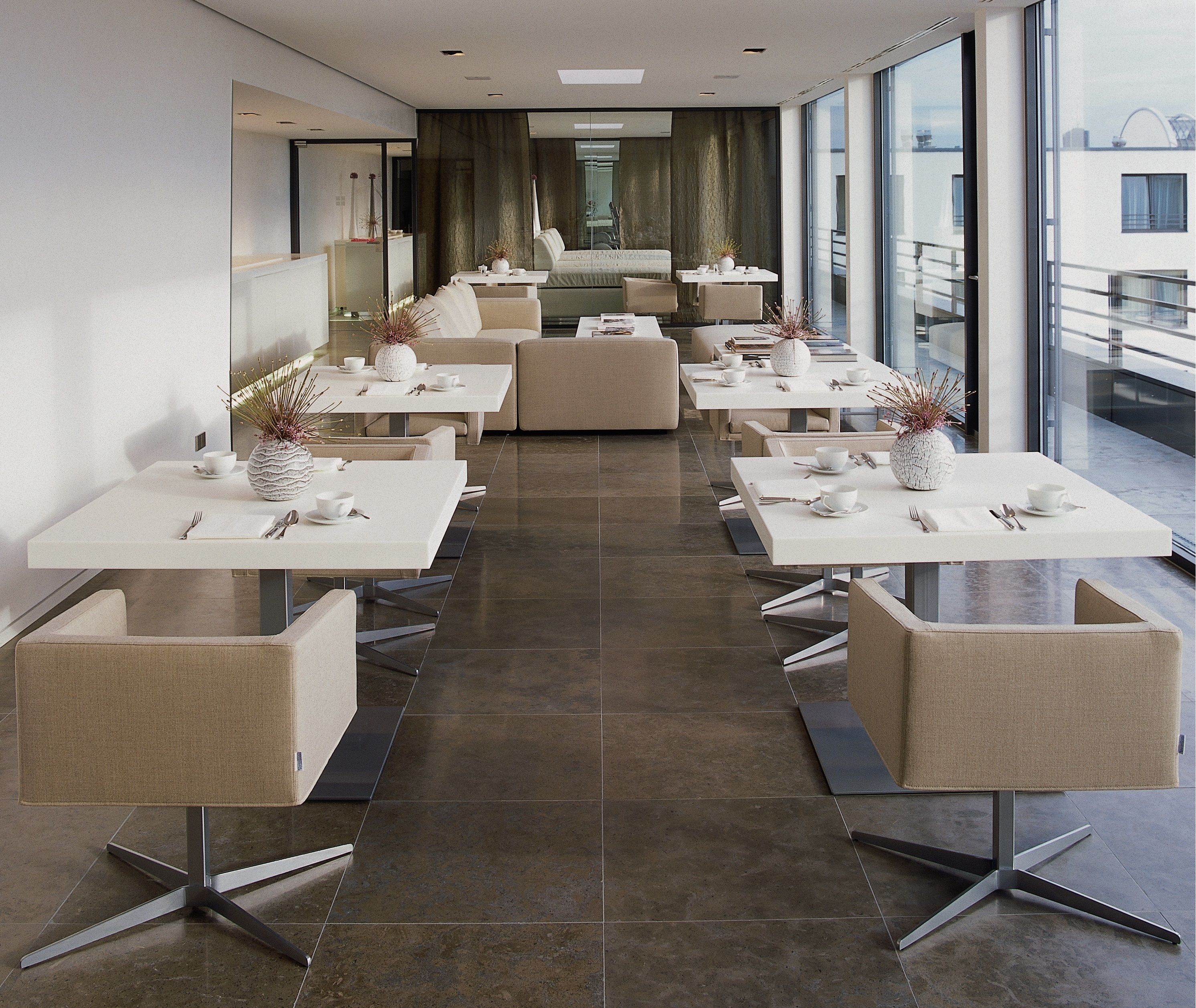 Een moderne eetruimte met meerdere tafels en stoelen, een stadszicht door grote ramen en een trap naar een hoger niveau.