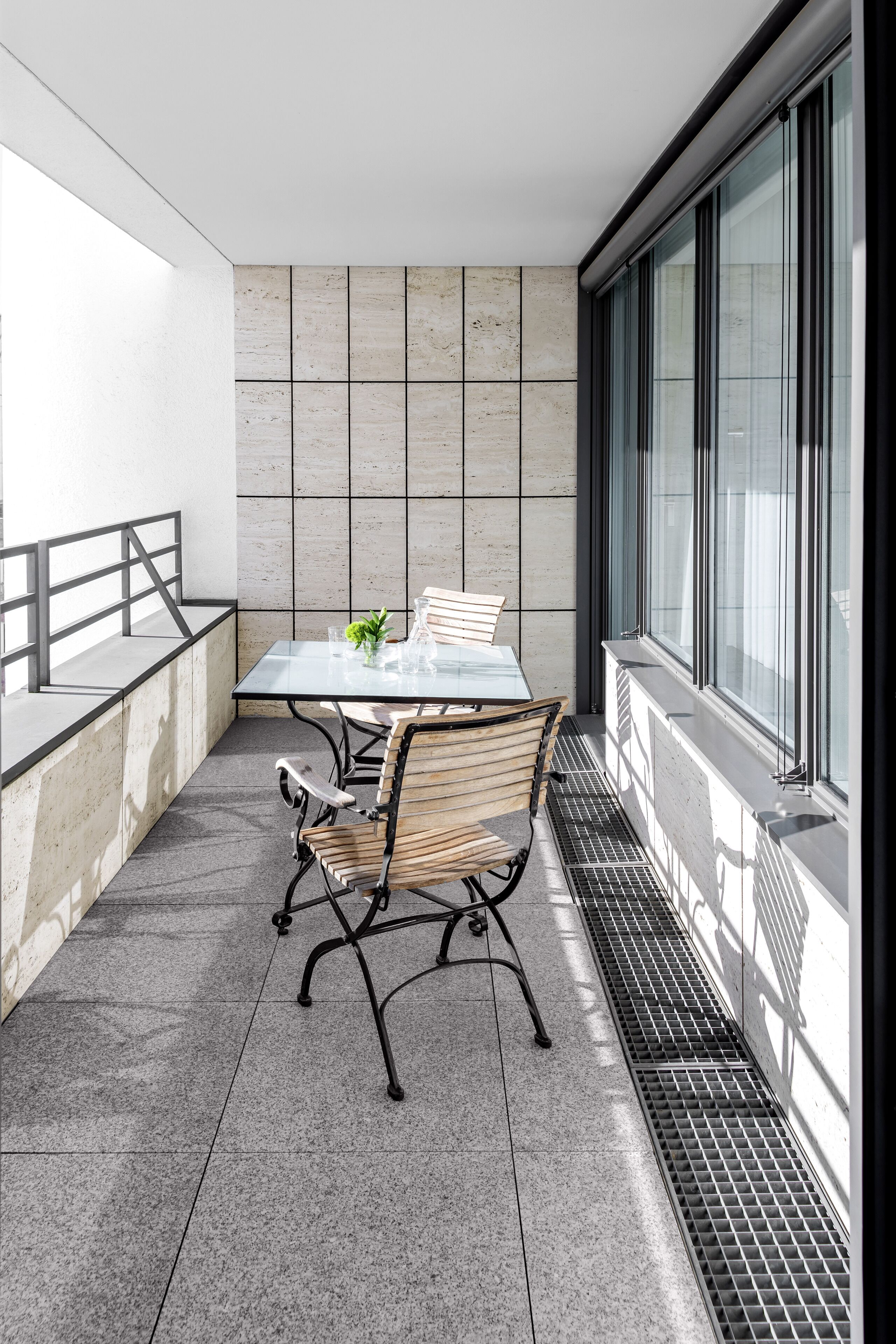 Un balcón moderno con una mesa de vidrio, sillas de metal y vistas a la ciudad.