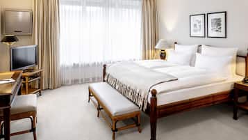A hotel room with a large bed, a desk with a computer, a bench, and two framed pictures on the wall.