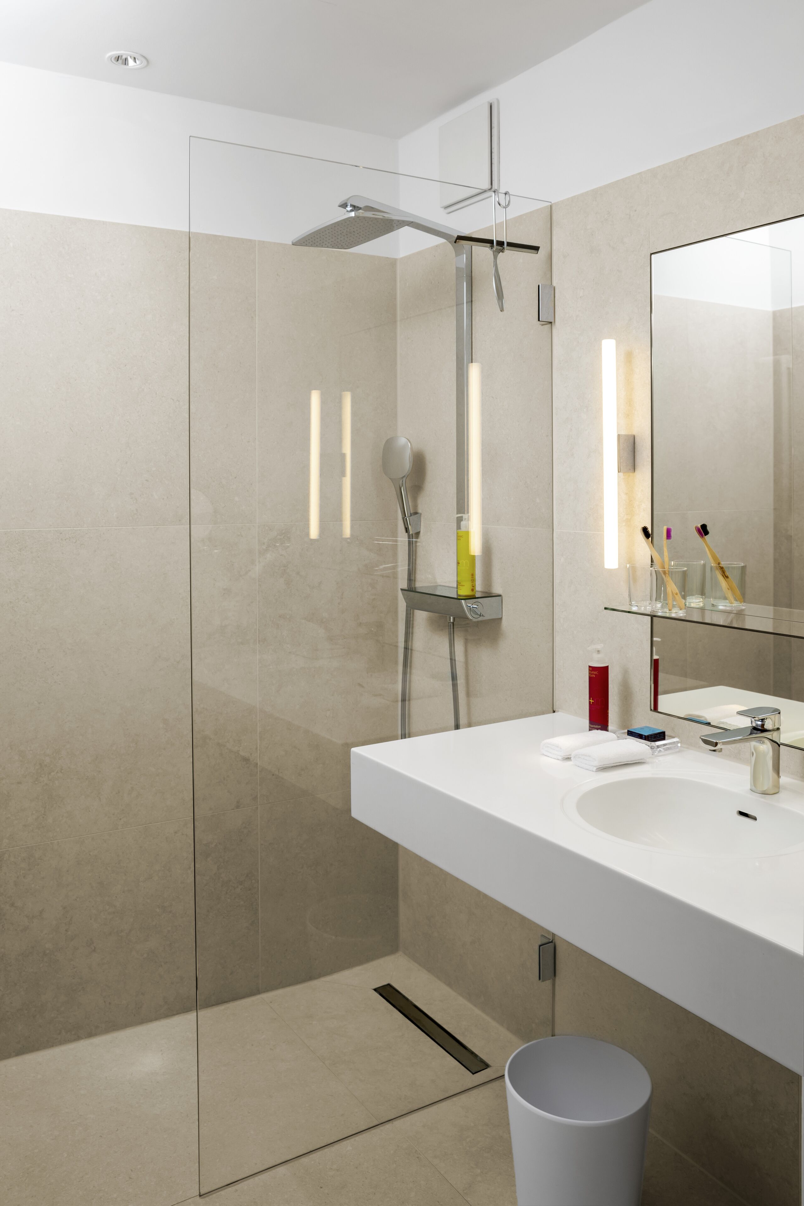 Un baño moderno con cabina de ducha de vidrio, un lavamanos blanco y un espejo con luz integrada.