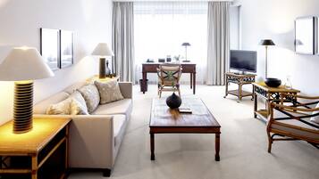 Una habitación de hotel moderna con sofá, una mesa de centro de madera, televisor y escritorio con computadora y lámpara.