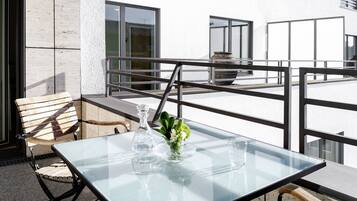 A glass-top table with a vase of flowers and a glass pitcher on a balcony with a railing.