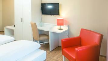 Ein Hotelzimmer mit einem Bett, einem Schreibtisch mit Stuhl, einem roten Sessel, einem Kleiderschrank und einem an der Wand befestigten Fernseher.