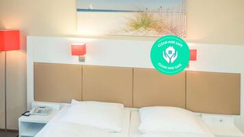 A hotel room with a bed, bedside tables, a phone, and a painting of a beach scene.