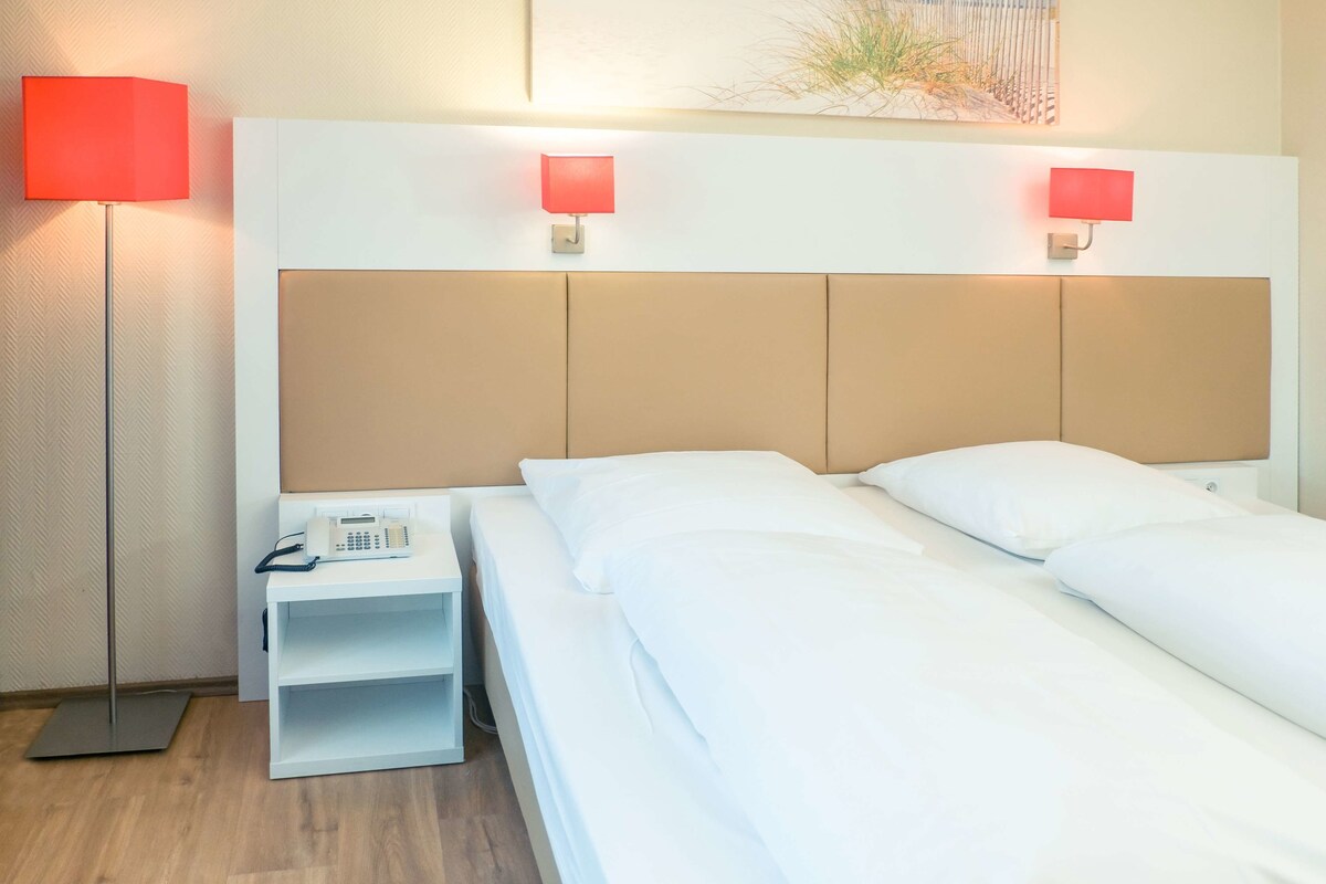 A hotel room with a bed, bedside tables, a telephone, and two wall-mounted lamps.
